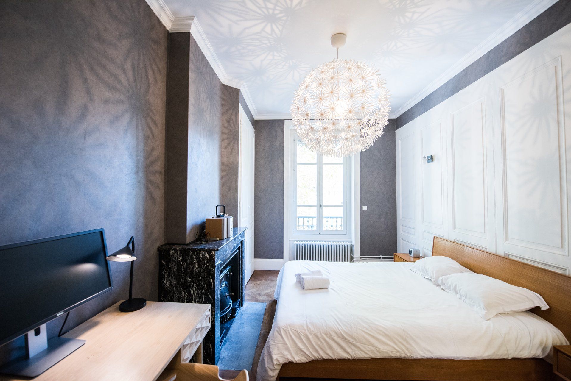 A hotel room with a bed, a desk with a computer, a dresser, and a chandelier.