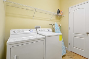 A laundry area with two white washing machines, a drying rack, and a door with a towel hanging on it.
