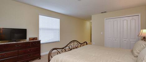 Un dormitorio con cama, cómoda, televisor, ventana con persianas y una puerta.