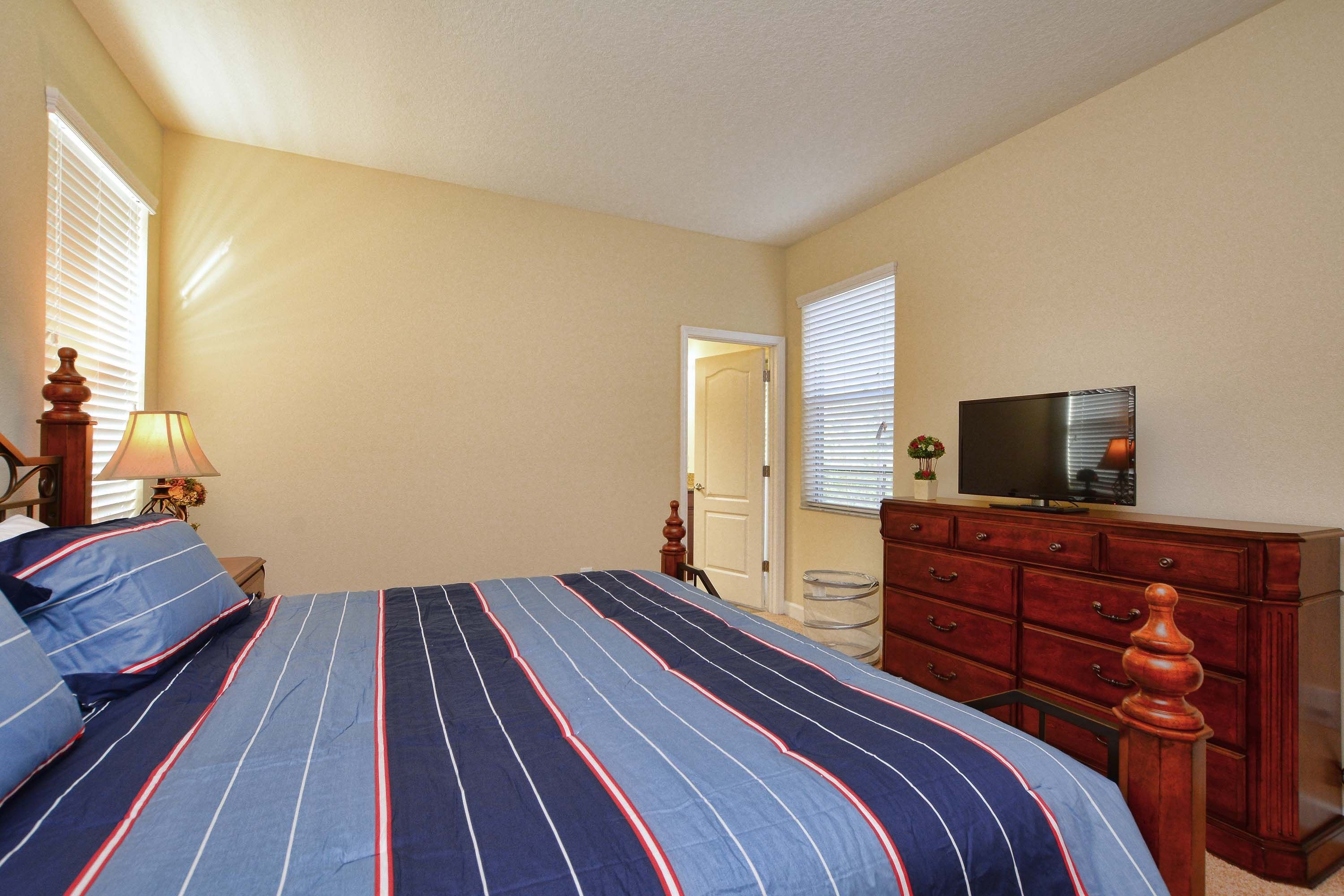 A bedroom with a bed, dresser, television, and a door leading to another room.
