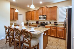 A kitchen with wooden cabinets, granite countertops, a central island with chairs, and modern appliances.