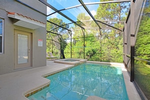 A covered swimming pool with a glass enclosure, a door, and a warning sign.
