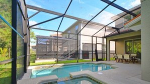 A swimming pool with a glass enclosure, surrounded by a patio area with chairs and a table.