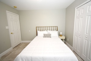 A bedroom with a bed, nightstand, and two doors. - Greater Groves - 5 Bedrooms House w/pool-5202GG Home by RedAwning (Clermont)
