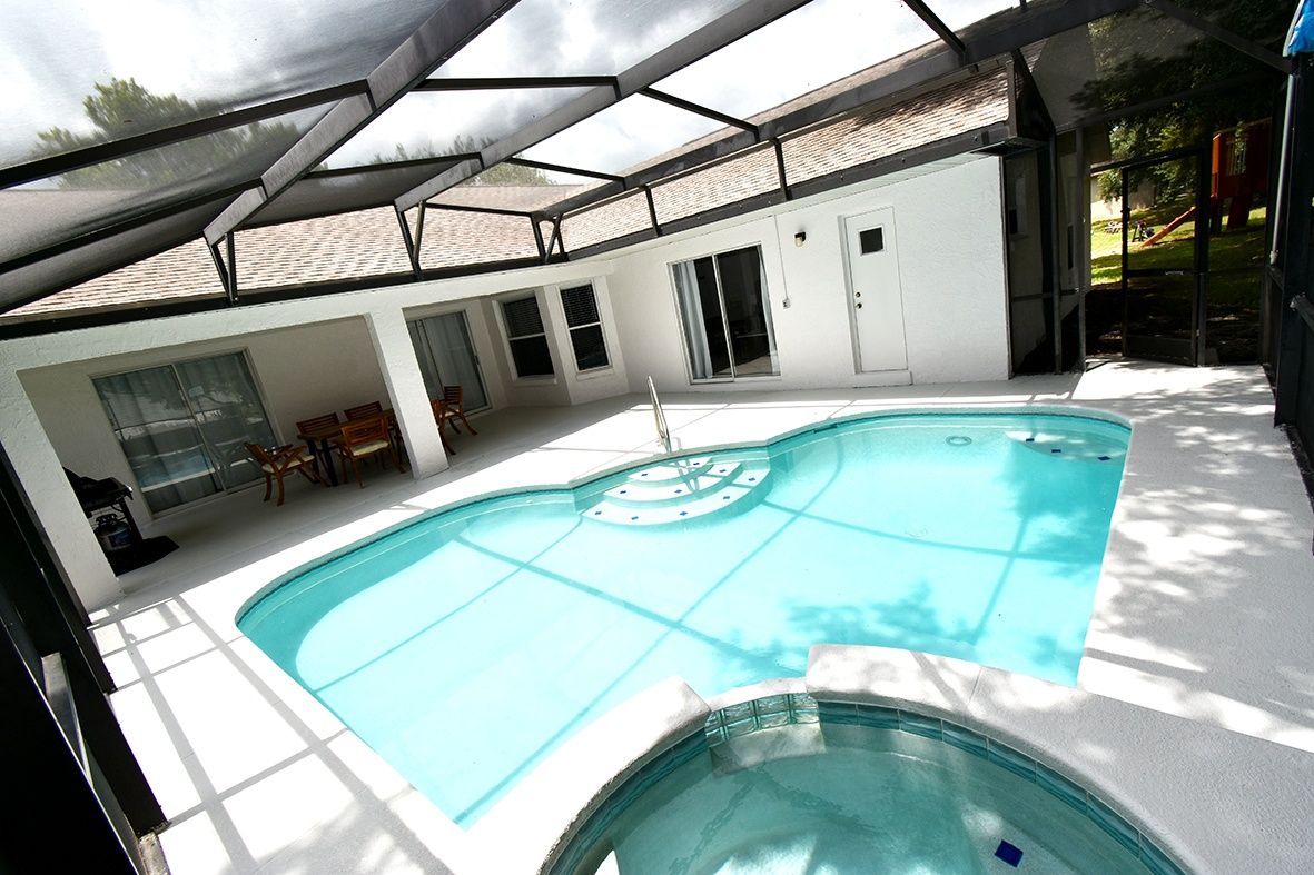Una piscina con una estructura de sombrilla, una zona de estar cubierta y vistas a un parque infantil.