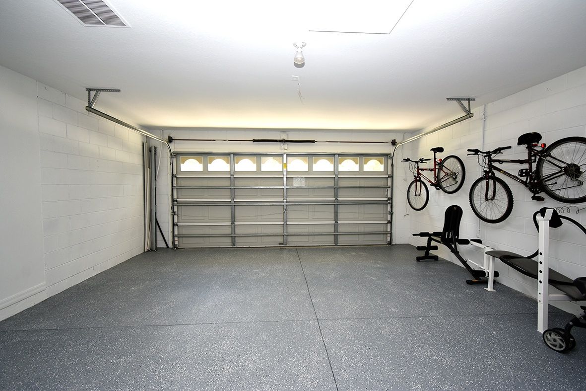 A garage with a closed garage door, exercise equipment, and bicycles mounted on the wall.
