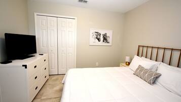 Un dormitorio con cama, cómoda, televisor, mesita de noche, lámpara y puerta.