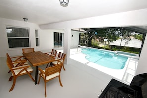 A modern outdoor dining area with a pool, white walls, and a clear view of the backyard. - Greater Groves - 5 Bedrooms House w/pool-5202GG Home by RedAwning (Clermont)