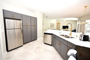 A modern kitchen with grey cabinets, stainless steel appliances, and a white countertop. - Greater Groves - 5 Bedrooms House w/pool-5202GG Home by RedAwning (Clermont)