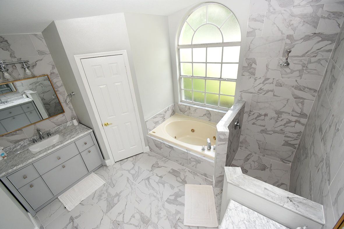 A bathroom with a marble floor, a bathtub, a sink with a mirror, and a window.