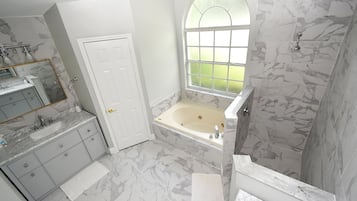 A bathroom with a marble floor, a bathtub, a sink with a mirror, and a window.