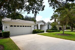 A single-story house with a garage, a front yard with a lawn, and mature trees. - Greater Groves - 5 Bedrooms House w/pool-5202GG Home by RedAwning (Clermont)