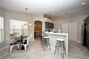 A modern kitchen with a central island, bar stools, and a dining area with a round table and chairs. - Greater Groves - 5 Bedrooms House w/pool-5202GG Home by RedAwning (Clermont)