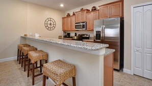 A kitchen with wooden cabinets, stainless steel appliances, a granite countertop, and woven stools. - Paradise Palms-4 Bed W/splashpool-3610pp 4 Bedroom Townhouse by RedAwning (Kissimmee)