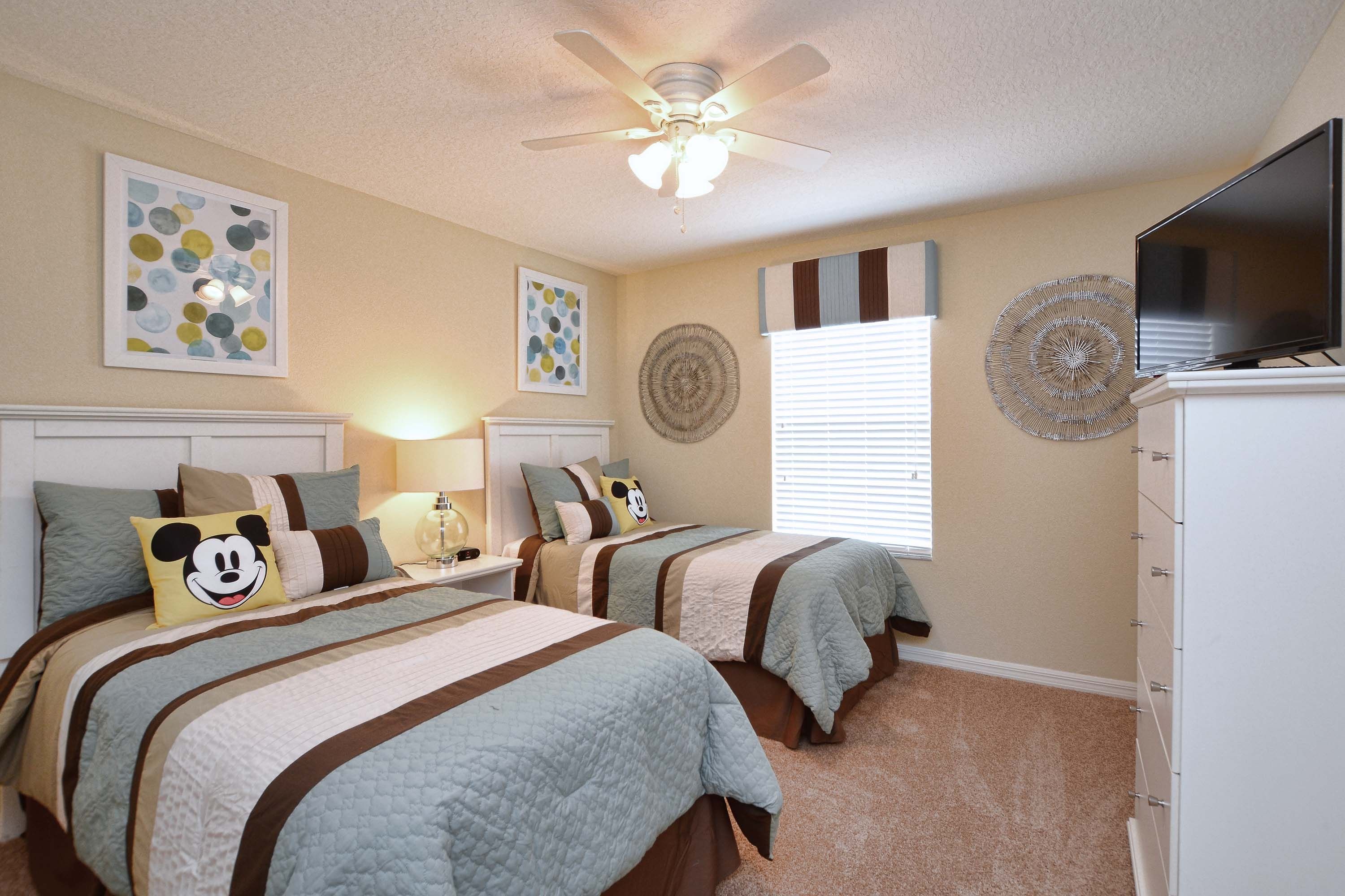 A bedroom with two beds, a ceiling fan, artwork on the walls, and a television on a dresser.