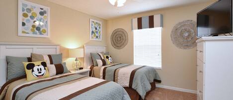 A bedroom with two beds, a ceiling fan, artwork on the walls, and a television on a dresser.