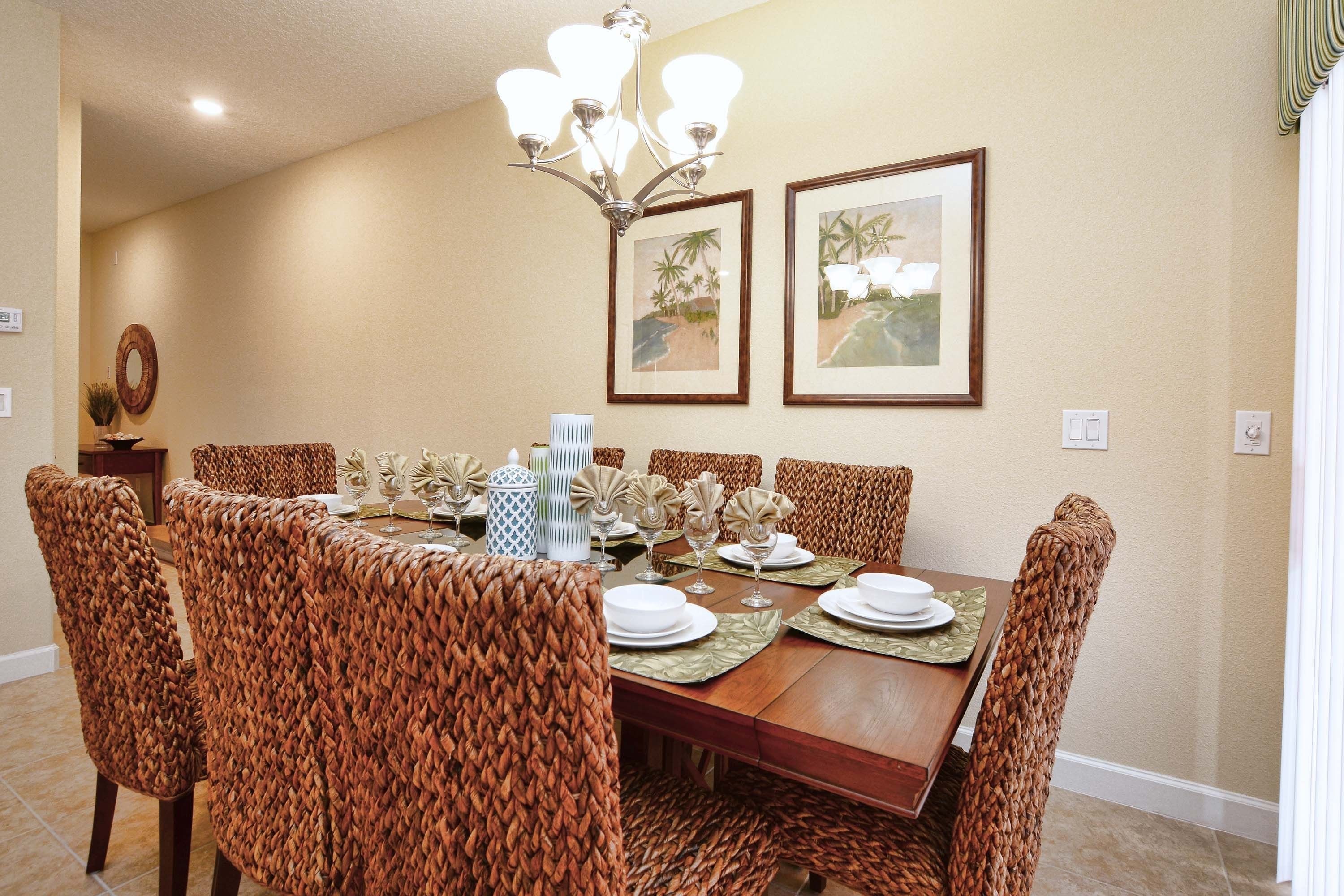 A dining area with a wooden table, woven chairs, and framed artwork on the wall.