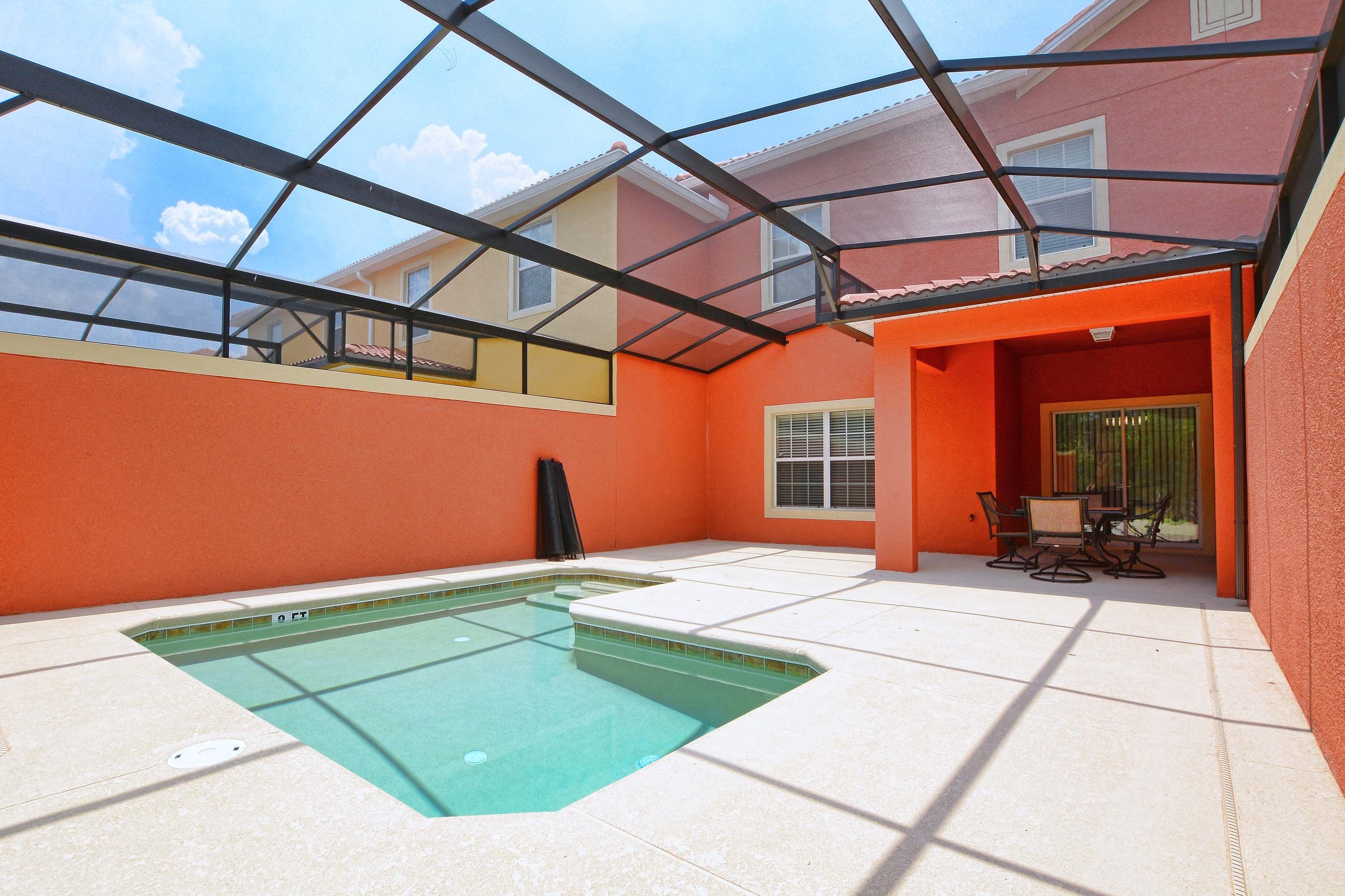 A swimming pool with a glass ceiling, surrounded by orange walls and a patio area with outdoor furniture.