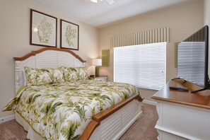 Un dormitorio con una cama, una mesita de noche, una lámpara, un televisor y una ventana con persianas.