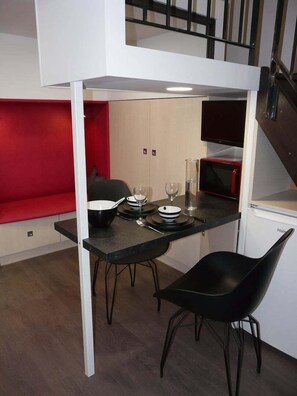 A compact kitchenette with a microwave, a small refrigerator, and a dining area with two black chairs and a table set with plates, bowls, and glasses.