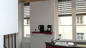 Et lille køkken med en rød bordplade, en hvid vask og en kaffemaskine på en hylde.