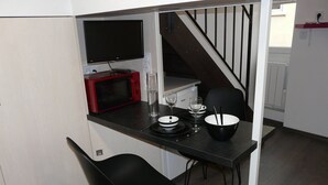 Et kompakt køkken med indbygget TV, mikrobølgeovn og et spiseområde med to stole og et bord dækket til to personer.