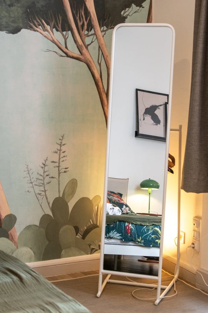 A room with a bed, a standing desk, a green lamp, and a mural on the wall.
