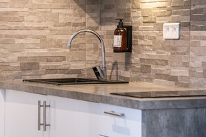 Una cocina con un lavamanos de acero inoxidable, un dispensador de jabón y un interruptor de luz en la pared.