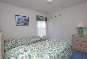 A bedroom with two beds, a window with curtains, a door, a dresser, and a painting on the wall.