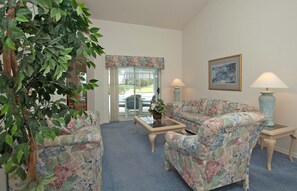A living room with floral upholstery, a glass door leading outside, and two lamps on side tables. - Greater Groves-4 Bedrooms Home W/pool-5204GG Home by RedAwning (Clermont)