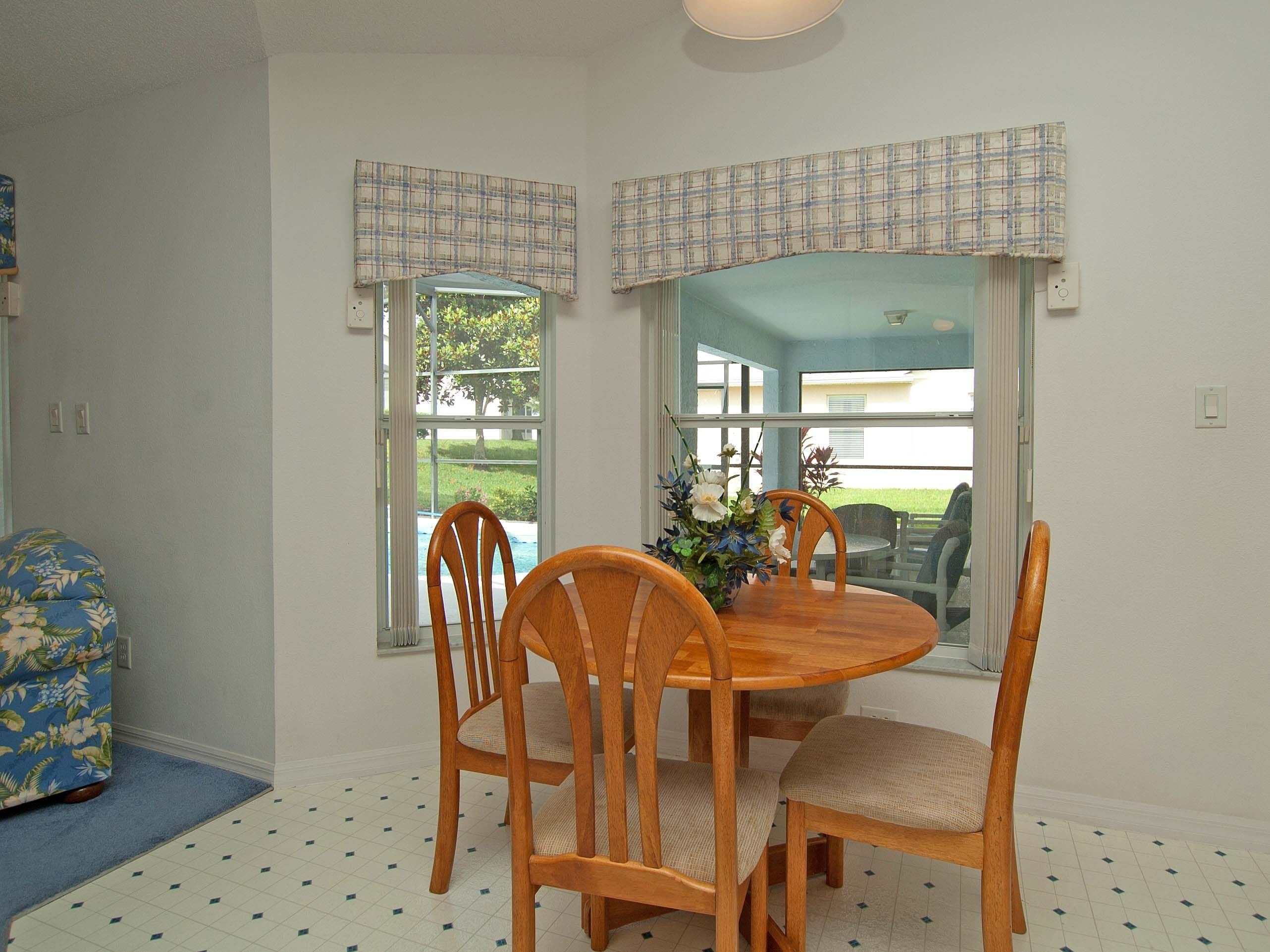 A dining area with a wooden table and chairs, a vase with flowers, and a view through a window.