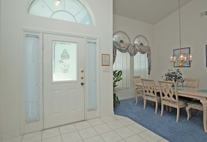 A dining area with a wooden table and chairs, a chandelier, and a large window with curtains. - Greater Groves-4 Bedrooms Home W/pool-5204GG Home by RedAwning (Clermont)