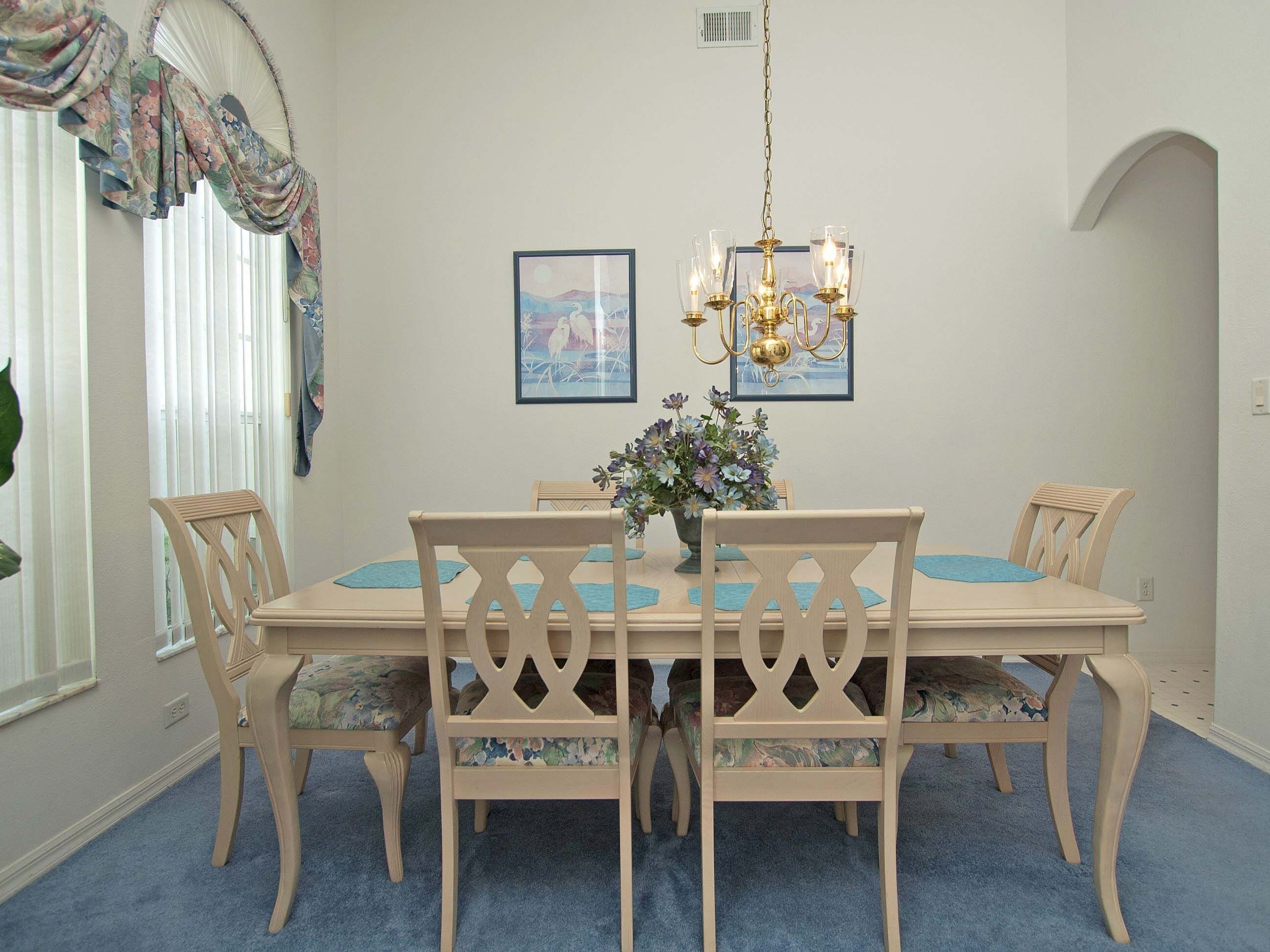 A dining room with a wooden table, chairs, a chandelier, and two framed pictures on the wall.