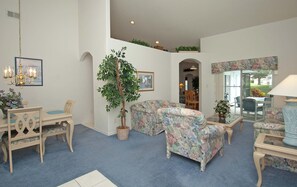 A living room with a blue carpet, floral sofa, wooden chairs, a dining table, and a chandelier.