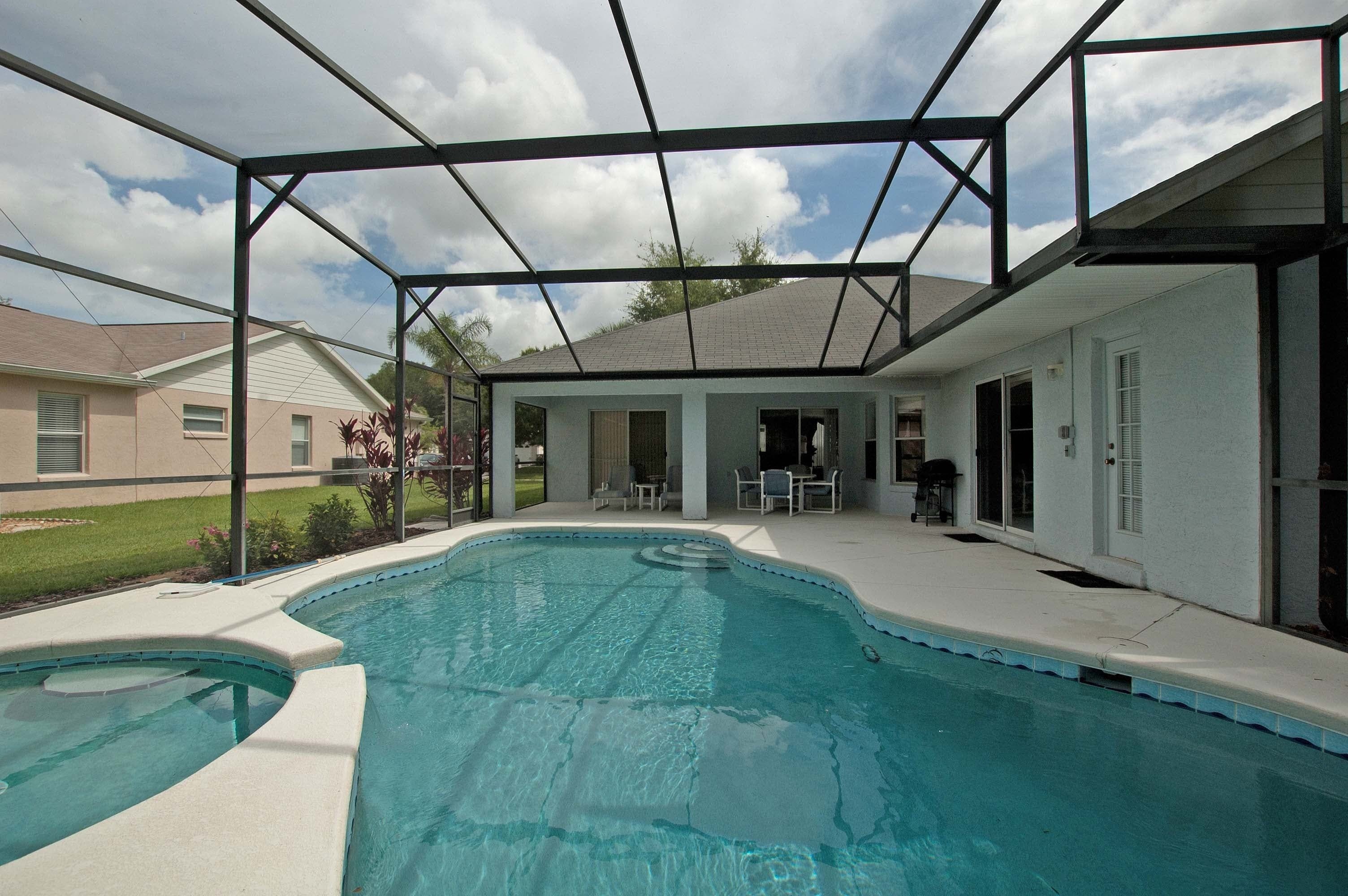 A swimming pool with a covered patio area, a lawn, and a neighboring house.