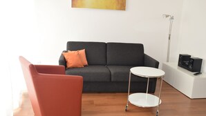 A modern living room with a grey sofa, a red armchair, a small white table, and a floor lamp. - Nice apartment on the ground floor for 2 persons (Höxter (Lüchtringen))