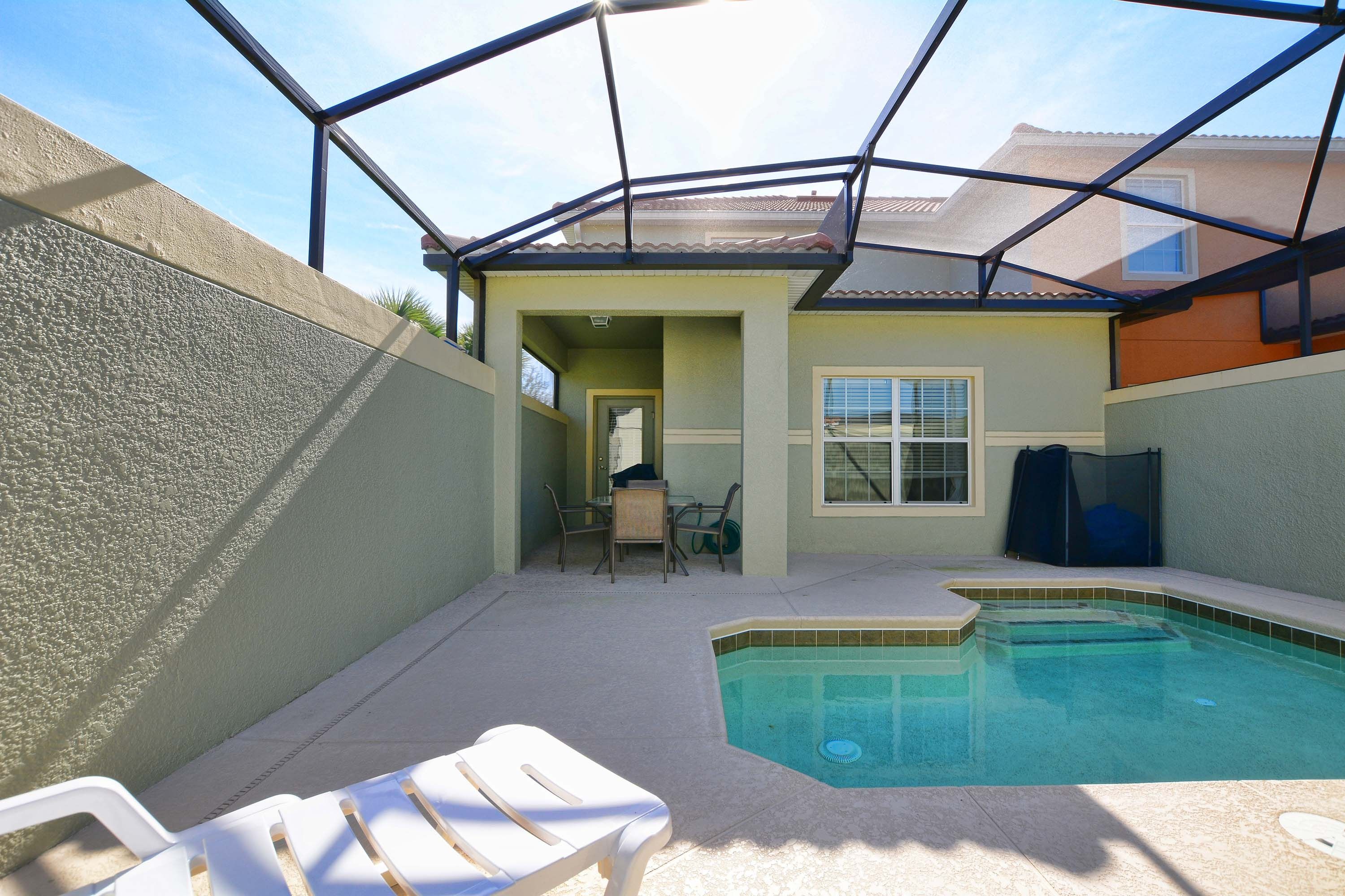 A swimming pool with a glass enclosure, a patio area with chairs, and a door leading to a covered porch.