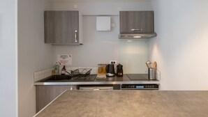 A compact kitchen with a built-in dishwasher, a coffee maker, and a kettle on the countertop. - Le cocon des Monts d'Or - cosy studio (Saint-Germain-au-Mont-d’Or)