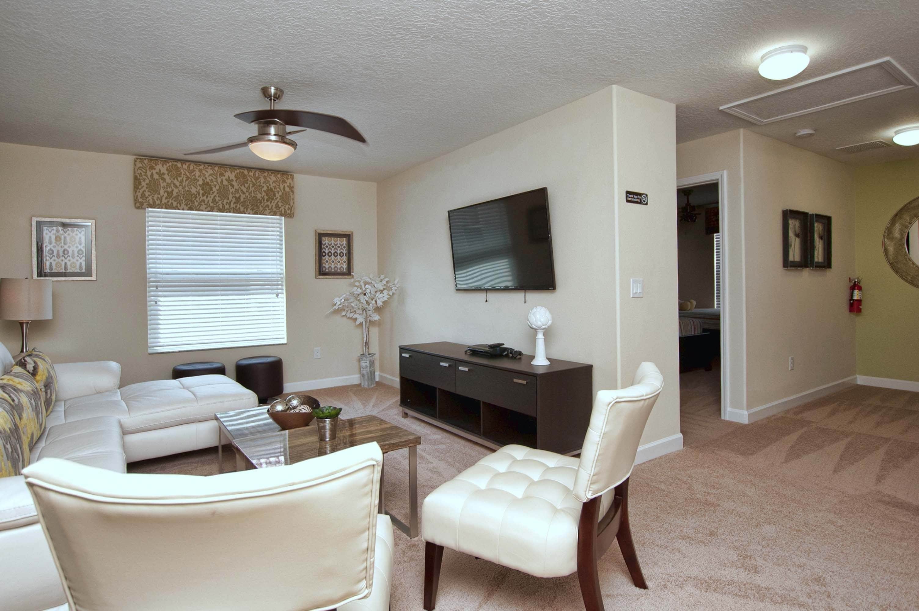 A living room with a sofa, armchair, coffee table, TV, and a ceiling fan.