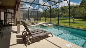 A pool area with lounge chairs and a hot tub, surrounded by a glass enclosure with a view of a grassy landscape.