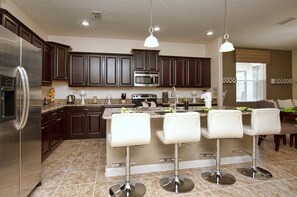 A modern kitchen with dark wooden cabinets, stainless steel appliances, and a central island with bar stools.