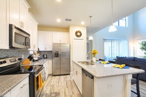Una cocina moderna con una isla central, electrodomésticos de acero inoxidable y una zona de comedor con sofá y mesa.