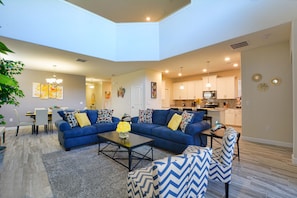 A modern living room with a blue sofa set, a coffee table, and a dining area with a table and chairs. - Solterra - 5 Bedrooms House w/pool-7035SR Home by RedAwning (Davenport)