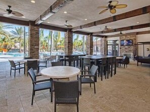 A spacious indoor area with multiple tables and chairs, a pool visible through large windows, and ceiling fans. - Solterra - 5 Bedrooms House w/pool-7035SR Home by RedAwning (Davenport)