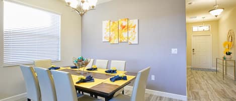 A dining area with a table set for six, chairs, a chandelier, and a wall-mounted painting.