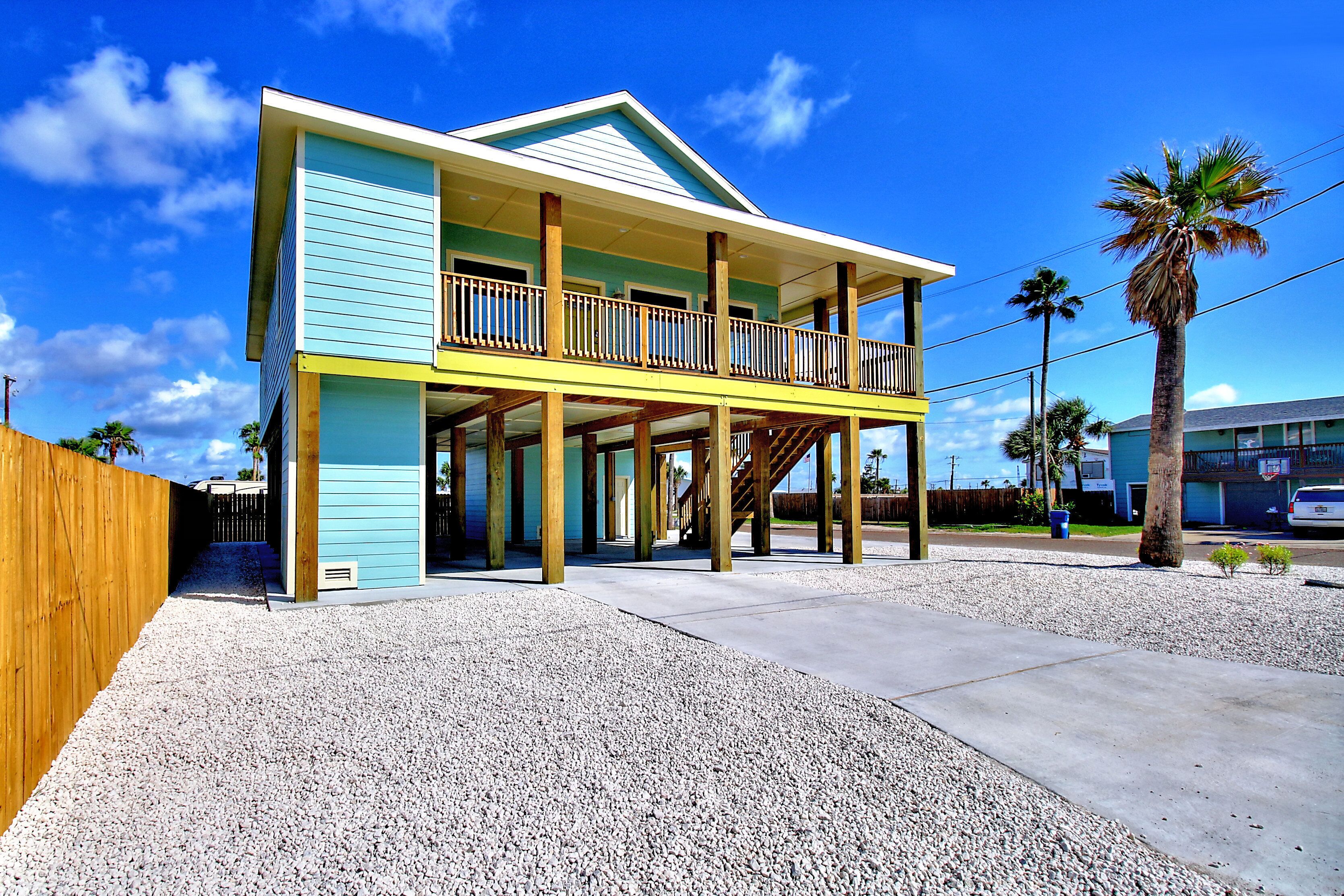 A two-story building with a balcony, wooden columns, and a gravel driveway.