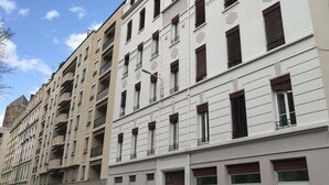 A multi-story building with white facades and red shutters, featuring balconies and a red door.