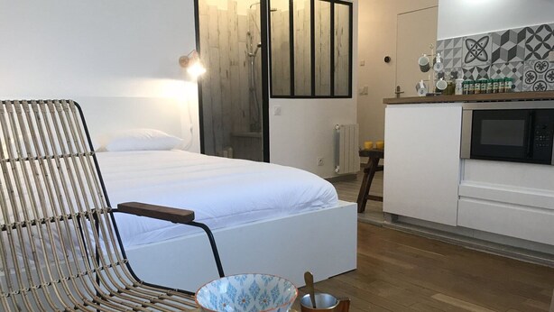 A modern bedroom with a large bed, a wicker chair, and a dining table with bowls and a cup.