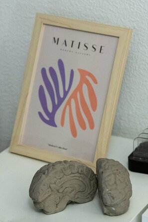 Un'opera d'arte incorniciata con la scritta 'MATISSE' e forme astratte, due oggetti a forma di cervello su una superficie bianca.