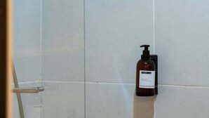Ein Badezimmer mit Dusche, gefliesten Wänden und einer Shampoo-Flasche an der Wand.